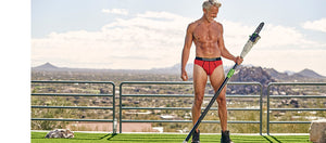 Men's underwear model in a red brief holding a tree trimmer chainsaw looking thrilled
